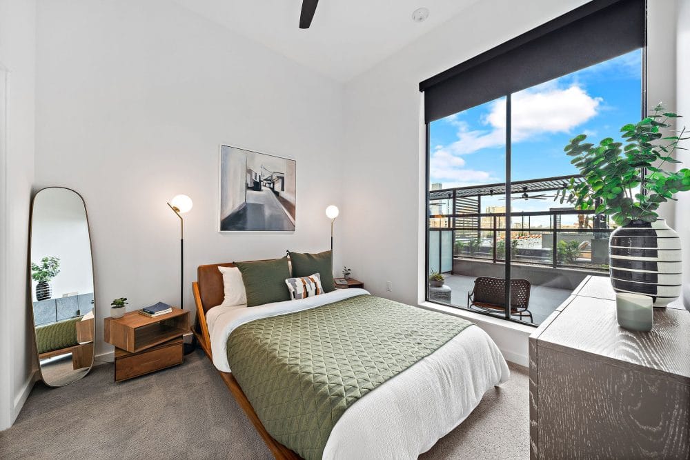 apartment bedroom with carpeting, a ceiling fan, and a large window overlooking a private balcony