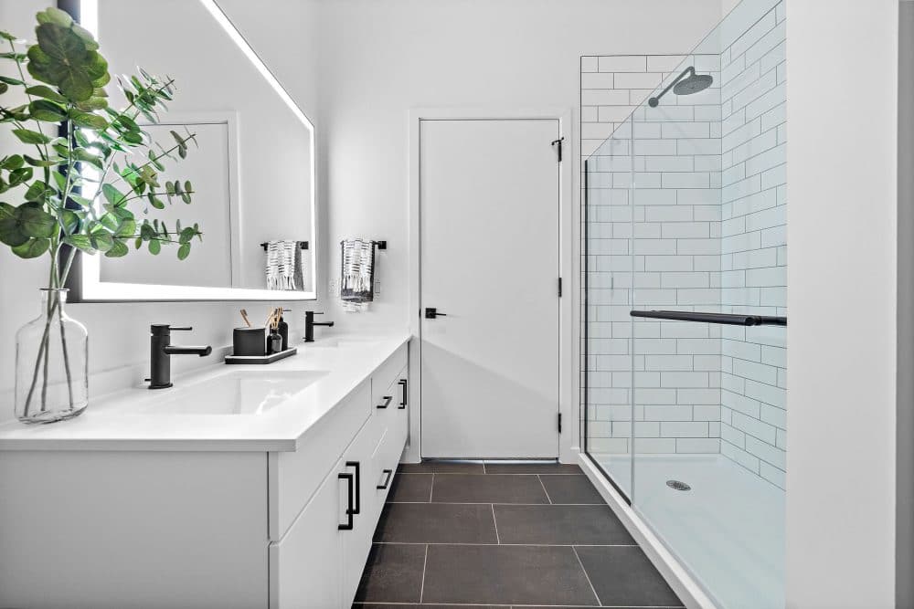 Forth at Navigation Apartments bathroom featuring a walk-in shower, front lit mirror, and double vanity