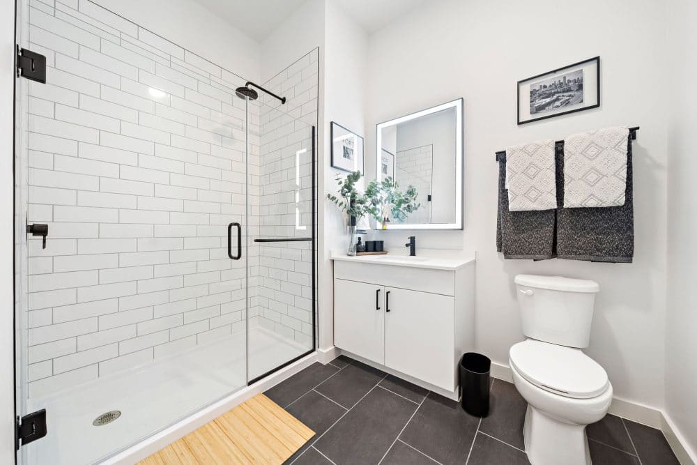 apartment bathroom with a glass walk-in shower, lit bathroom mirror, and floating vanity at Forth at Navigation Apartments