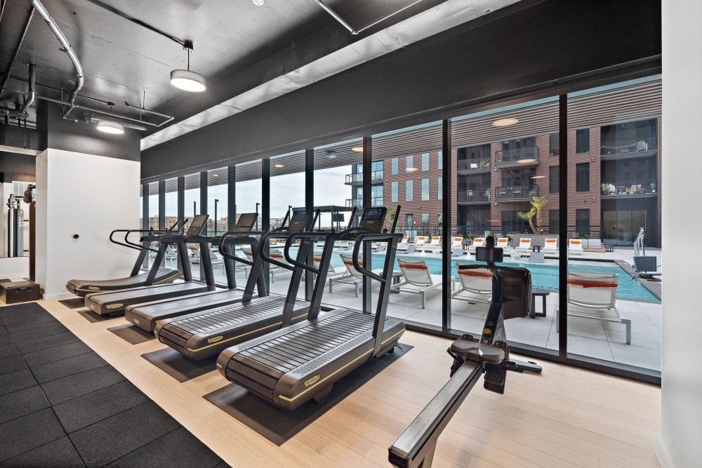 treadmills lined up against a floor-to-ceiling window overlooking the outdoor swimming pool